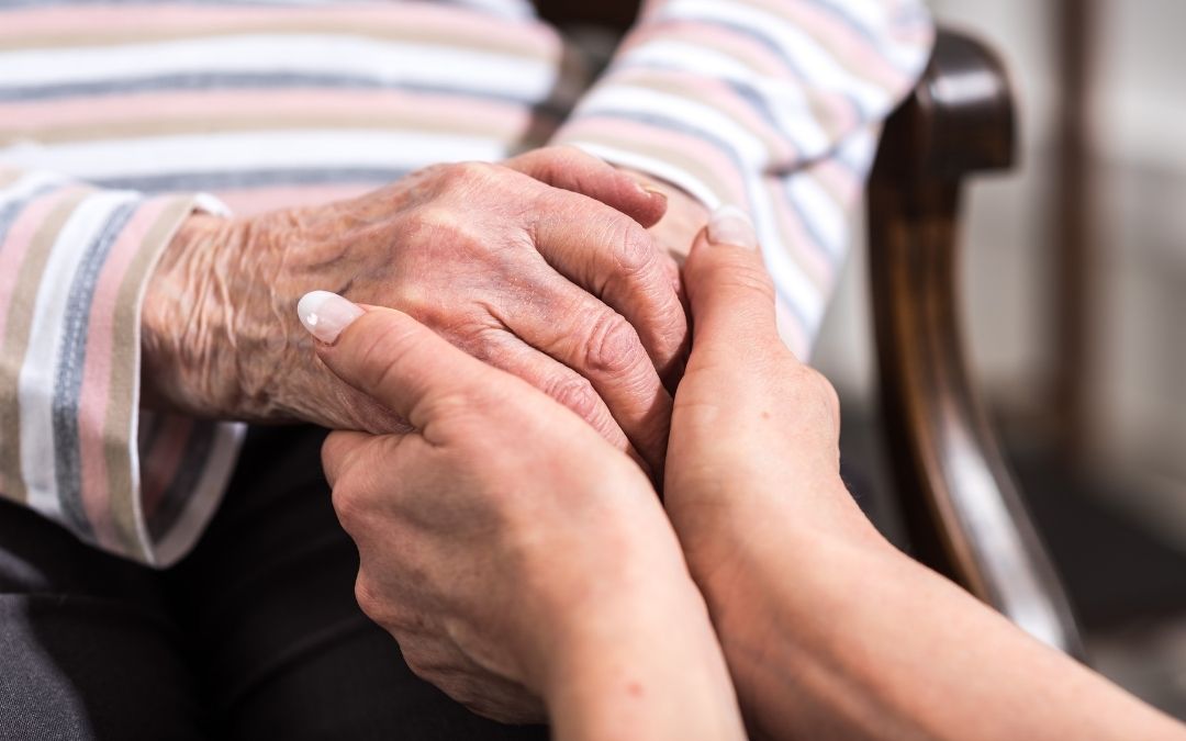 Adult Child Holding Hands with Elderly Parent in Assisted Living Home